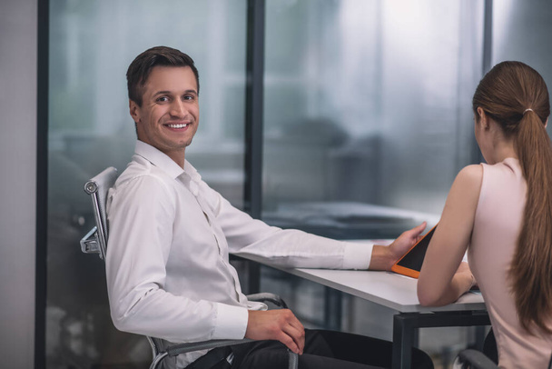Smiling dark-haired male sitting at table with his female colleague - Photo, Image