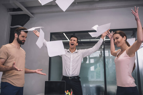 Happy female and two male coworkers tossing papers - Fotografie, Obrázek