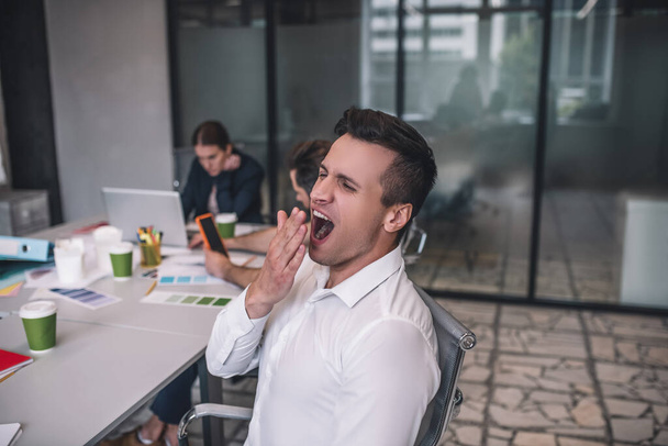 Tired dark-haired male sitting at meeting, yawning - 写真・画像