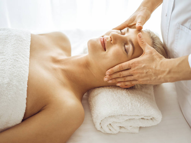 Beautiful blonde woman enjoying facial massage with closed eyes. Relaxing treatment in medicine and spa center concepts - Φωτογραφία, εικόνα