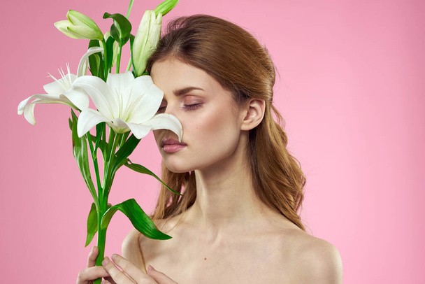 mooie vrouw met boeket van bloemen in handen blote schouders roze achtergrond charme - Foto, afbeelding