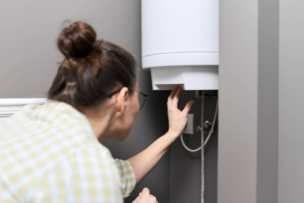 Home water heater, woman regulates the temperature on an electric water heater - Fotoğraf, Görsel