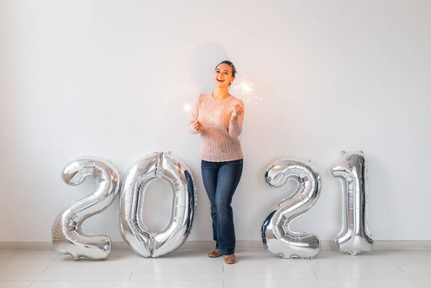 新年のお祝いとパーティーのコンセプト-白い背景にシルバー2021風船の近くに輝きを持つ幸せな若い女性. - 写真・画像