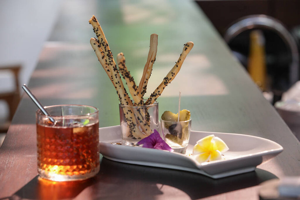 Соленые палочки и чай со льдом на столе ресторана. - Фото, изображение