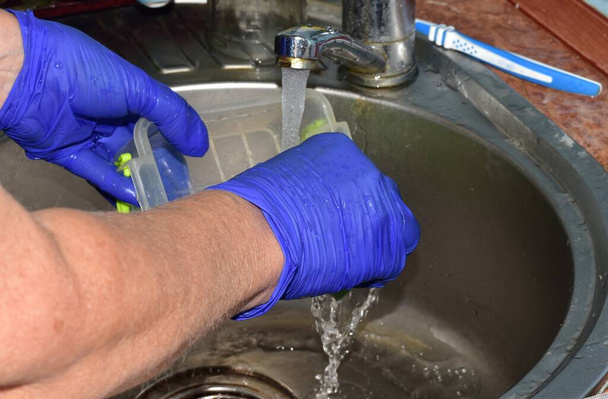 Una mujer lava un cuenco de plástico con agua fría. - Foto, imagen