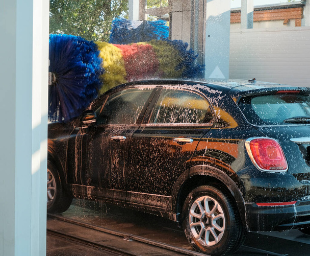 A fekete autót automata autómosóban mossák. Autómosó szolgáltatás közelkép.  - Fotó, kép