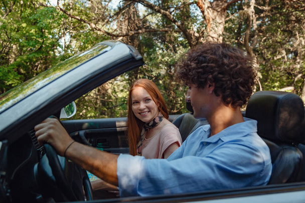 Couple enjoying a drive in a convertible in summer road. Friends going on holidays. Italian vacation serpentine roads, a redheaded woman and a beautiful young man - Φωτογραφία, εικόνα