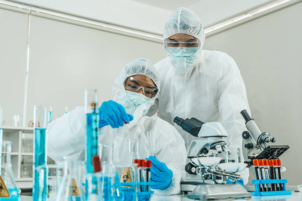 Deux scientifiques en costume EPI travaillent en laboratoire tout en vérifiant les résultats des analyses d'échantillons de sang. Blue Tone. SRAS-CoV-2, Covid-19 THÈME. - Photo, image
