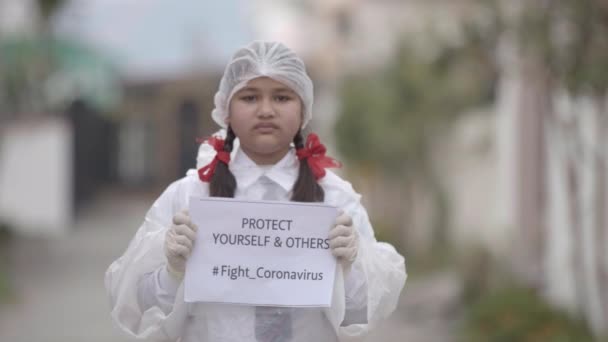 COVID-19 Coronavirus- smrtící virus: Dívka v masce, rukavicích a ochranných šatech ve školní uniformě pro bezpečnost proti COVID-19 Coronavirus. Apple ProRes 422.Dívka šířící povědomí - Záběry, video