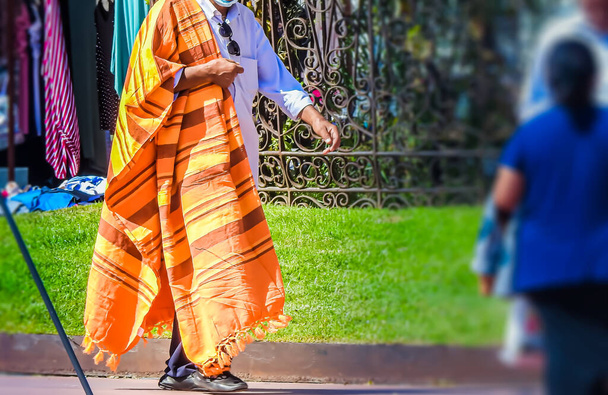 Uomo con un materiale arancione sulle spalle che cammina per il mercato per venderlo - Foto, immagini