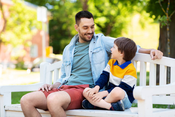 father with son sitting on park bench and talking - Foto, Imagen