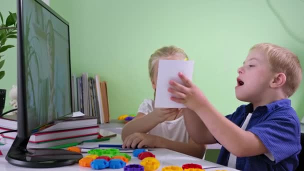 gyermek Down-szindróma otthon oktatás, lány segít a testvérének egy online órát tanár a képernyőn számítógép ül az asztalnál - Felvétel, videó