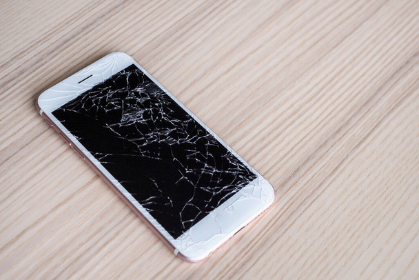 σπασμένο γυαλί της οθόνης του κινητού τηλεφώνου σε ξύλινο φόντο - Φωτογραφία, εικόνα