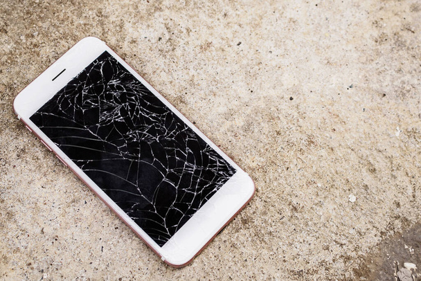 разбитое стекло экрана мобильного телефона на бетонном фоне пола - Фото, изображение
