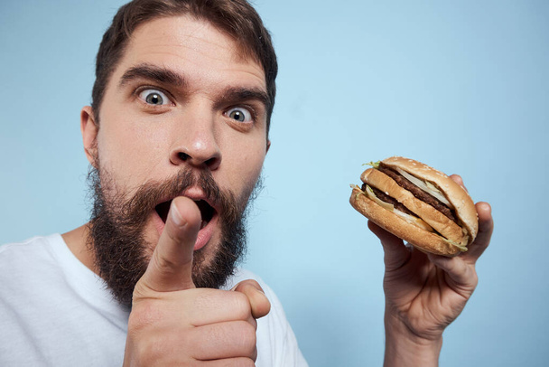 Hamburguesa hombre emocional comida rápida dieta primer plano fondo azul - Foto, imagen