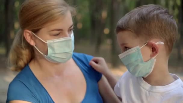 Matka i syn w maskach medycznych siedzący w parku - Materiał filmowy, wideo