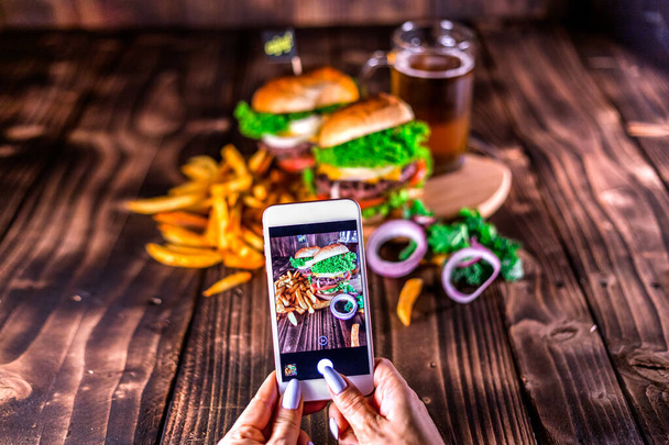 Žena, která dělá fotku se smartphonem ze sortimentu domácích hamburgerů. S barevnou čerstvou zeleninou. Zdravá výživa. Horní pohled. Dřevěné pozadí tabulky. - Fotografie, Obrázek
