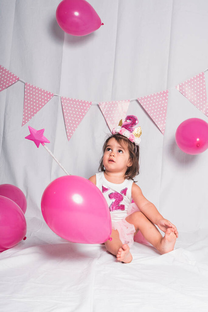 dívka sedící s hůlkou a růžovými balónky na bílém pozadí. Koncept narozenin - Fotografie, Obrázek