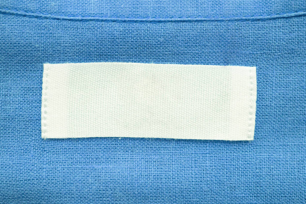 Etiqueta de etiqueta de ropa blanca en blanco sobre fondo de textura de camisa de lino azul - Foto, imagen