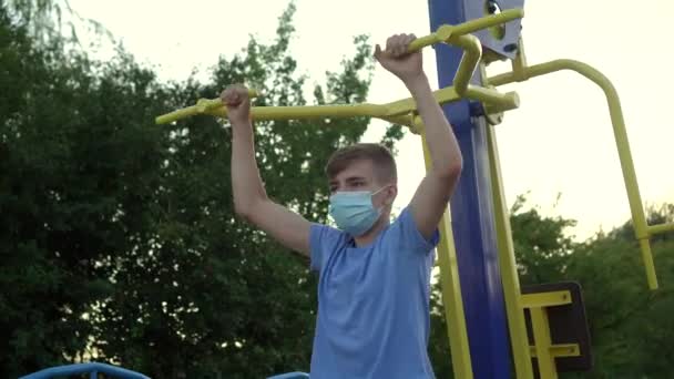 Un adolescente con máscara médica practica deportes en máquinas de ejercicio - Metraje, vídeo