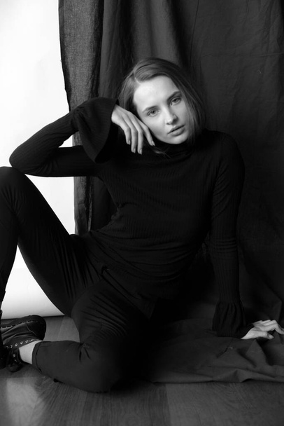 Young attractive girl model with blond hair and nude makeup in black knee-highs black trousers posing in the studio on a white and black background - Zdjęcie, obraz
