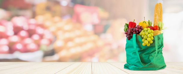Frutas y verduras frescas en bolsa de compras verde reutilizable en la mesa de madera con supermercado tienda de comestibles borrosa fondo desenfocado con luz bokeh - Foto, Imagen