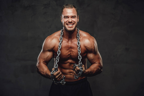 Człowiek z ogromnymi bicepsami i łańcuchami pozowanie w studio - Zdjęcie, obraz