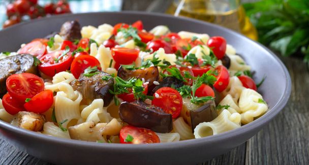 Pasta creste with grilled eggplant, cherry tomatoes and herbs. Delicious warm salad. Close up - Photo, Image