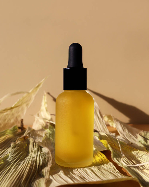 Cosmetic oil bottle, black dropper, dry leaves, beige background. Vertical mockup, banner, poster, copy space. Natural organic lotion, eco essence. Central composition, monochrome yellow brown colors - Foto, immagini