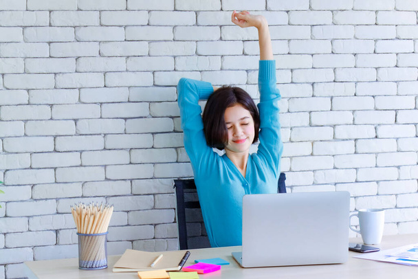 Young and cute half race Thai German woman sitting at working desk and stretch herself with hands over the head for relaxing and calm to get rid of lazy during long work in house. Work at home idea. - Photo, Image