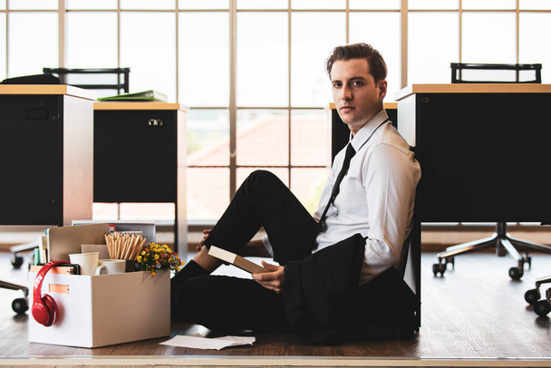 Young caucasian businessman in suit tired sitting with feeling sad, unhappy face holding family photo in frame in office at end job day. Idea for unemployed person, work crisis and get fired. - Фото, изображение