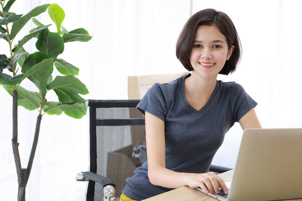 Fiatal, szép és gyönyörű félverseny Thai-német lány ül, és mosolyogni, mint az íróasztal használata közben labtop számítógép dolgozik a hálószobában otthon. Ötletek a boldogságért A fiatalok tanulnak és tanulnak otthonról. - Fotó, kép