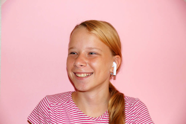 tizenéves lány hallgat zenét fejhallgató és mosolygós, portré rózsaszín háttér. - Fotó, kép