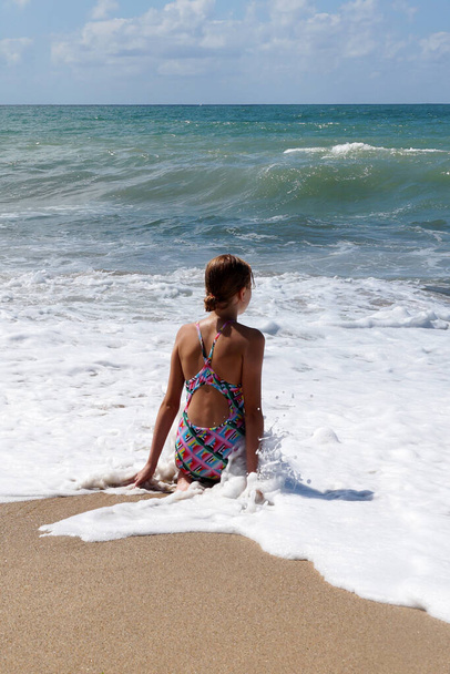 έφηβος κορίτσι κάθεται σε λευκό αφρό της θάλασσας και κοιτάζοντας τη θάλασσα. - Φωτογραφία, εικόνα