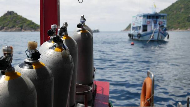 Wiersz zbiorników tlenu i sprzętu do nurkowania umieszczone na nowoczesnej łodzi w falującym oceanie w pobliżu kurortu Koh Tao, Tajlandia. Koncepcja sportów turystycznych ekstremalnych rozrywek, przygód i nowych doświadczeń - Zdjęcie, obraz