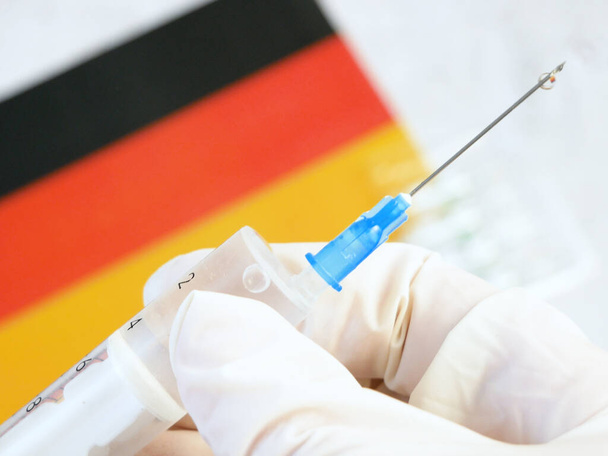 Spritze mit Impfstoff wird von Hand in einem Handschuh auf Hintergrund der Deutschland-Flagge gehalten, Impfung gegen Coronavirus, Nahaufnahme - Foto, Bild