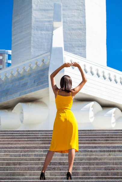 full-length portrait of a young beautiful woman in a summer dress posing against the backdrop of the rook monument in samara - Photo, image