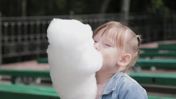 Hermosa y feliz niña comiendo algodón de azúcar en el banco. Joven madre feliz con niña. - Metraje, vídeo
