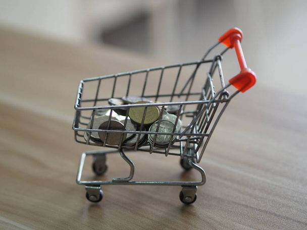 Coins money in mini model cart supermarket on wooden desk - Photo, Image