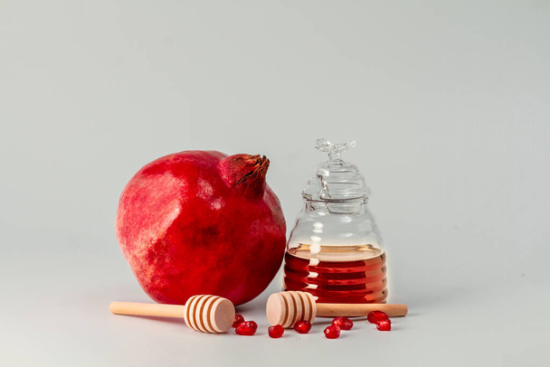 Ein Glas Honig, zwei Holzstäbchen für Honig und ein Granatapfel auf hellem Hintergrund. - Foto, Bild