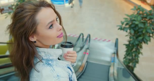 The girl is riding the escalator down and holding a cup of coffee. Close-up shooting. 4K - Footage, Video