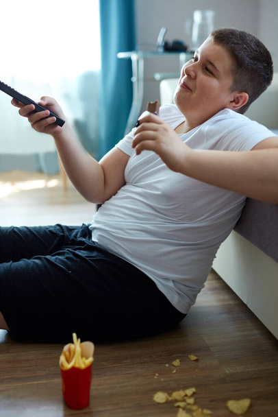 übergewichtiger dicker Junge isst Junk Food, während er allein zu Hause fernsieht - Foto, Bild