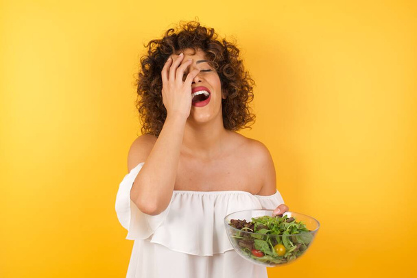 Charismatic carefree joyful friendly-looking outgoing woman holding a salad dressed casual likes laugh out loud not hiding emotions giggling hear funny hilarious joke chuckling facepalm close eyes smiling broadly  - Foto, afbeelding