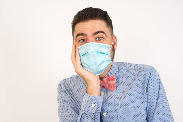 Surprise astonished handsome guy. Closeup portrait of man wearing medical mask looking surprised in full disbelief wide open mouth with hand near face. Positive emotion facial expression body language. Funny boy - Photo, Image