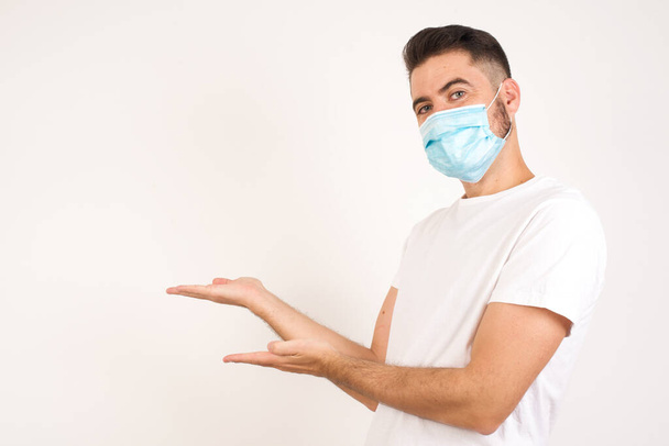 Young handsome caucasian man wearing medical mask over isolated background Inviting to enter smiling natural with open hands. Welcome sign. - Foto, imagen