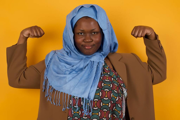 Vita alta colpo di donna afro-americana musulmana solleva le braccia per mostrare i suoi muscoli si sente fiducioso nella vittoria - Foto, immagini