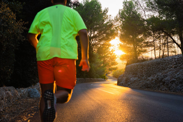 Paisagem de uma estrada no meio de uma floresta de pinheiros com belo pôr do sol dourado e homem desfocado correndo em direção ao sol - Foto, Imagem