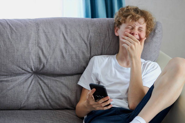 young redhead teen boy watching interesting videos on mobile phone - Foto, immagini