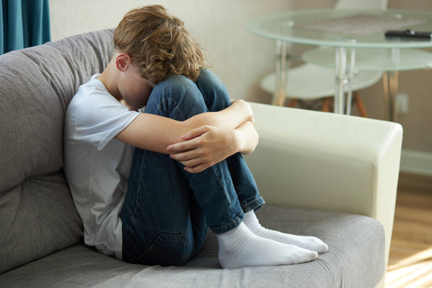 young caucasian teenage boy sitting alone on sofa, face down crying - Zdjęcie, obraz