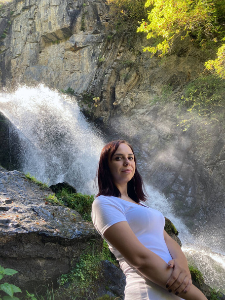 Portrait of young woman looking away on background of waterfall. Adult female tourist enjoying beautiful view in mountainous area. - Foto, Bild
